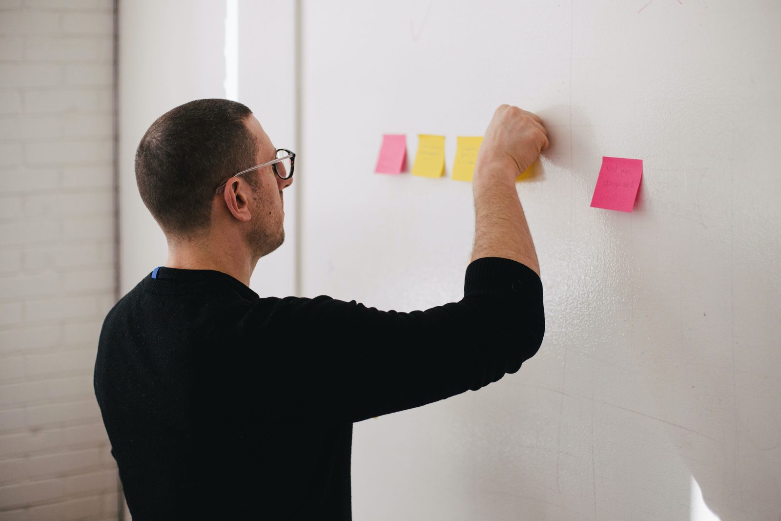 Designer placing sticky notes on a wall while synthesizing findings